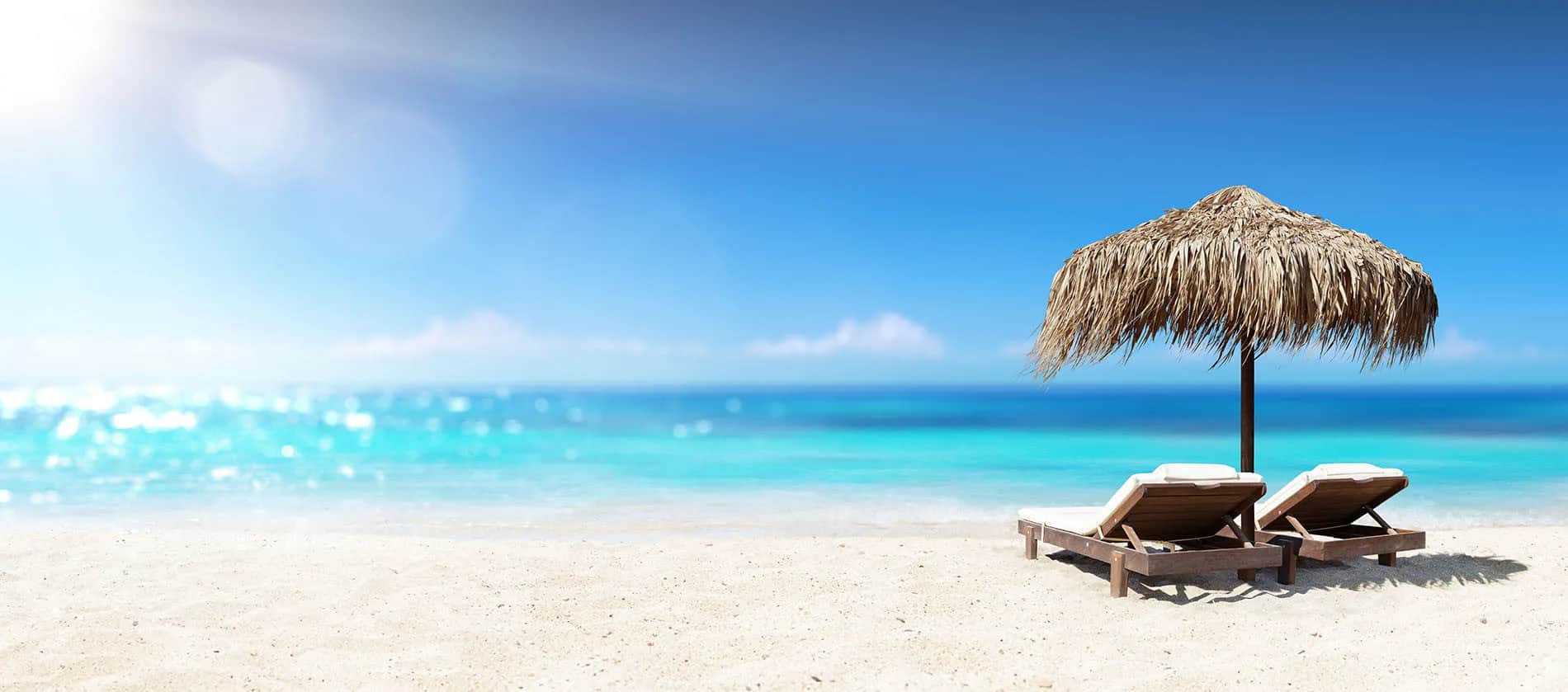 Luxury lounge chairs beneath a thatched umbrella facing crystal-blue waters