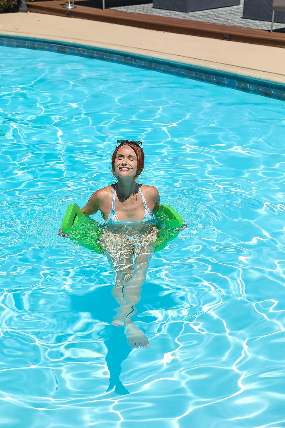 Woman floating upright in a green CocoCabana saddle pool float with a relaxed expression and eyes closed.

